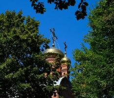 Dome of the Orthodox Church with crosses, view through the branches of trees against the blue sky photo
