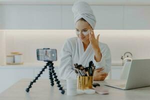 Young model promotes skincare product, applies eye patches, vlogs for blog, records video with smartphone. photo