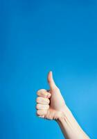 Realistic thumb up hand gesture on blue background with copy space. Like. Good feedback, positive reaction. Validation and approval. Empty space for text. Generative AI. photo