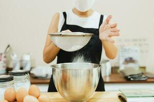 mujer panadero cernido harina dentro mezcla bol. foto
