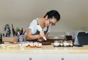 Woman pastry with a pastry bag in her hands squeezes cream on a cake in a bakery room. photo