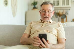 Happy middle aged senior man holding using smartphone touch screen typing scroll page. Stylish older mature beard grandfather with cell phone using internet social media apps at home. Shopping online. photo