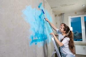 Pareja en nuevo hogar durante reparar trabajos pintura pared juntos. contento familia participación pintar rodillo pintura pared con azul color pintar en nuevo casa. hogar renovación bricolaje renovar hogar concepto. foto