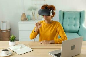 African american young woman wearing using virtual reality metaverse VR glasses headset at home. Girl touching air during VR experience on virtual reality helmet. Simulation hi-tech videogame concept. photo