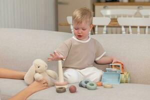 Happy family at home. Mother and baby boy playing with toys in couch at home indoors. Little toddler child and babysitter nanny having fun together. Young woman mom kid son rest in living room. photo