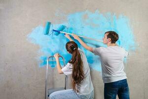 Pareja en nuevo hogar durante reparar trabajos pintura pared juntos. contento familia participación pintar rodillo pintura pared con azul color pintar en nuevo casa. hogar renovación bricolaje renovar hogar concepto. foto