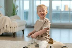 Happy child at home. Little toddler boy driving big vintage toy car and having fun. Smiling kid playing at home. Baby boy playing with toy in living room indoors. photo