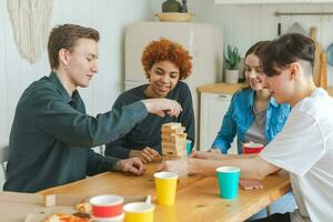 Home party. Friends spending time together playing in board game crash wooden tower at home. Happy diverse group having fun together indoor. Mixed race young buddies best friends enjoying weekend. photo