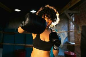 Women self defense power. African american woman fighter punching with boxing gloves to camera. Healthy strong girl punching training punches looking concentrated straight. Fit body workout. photo