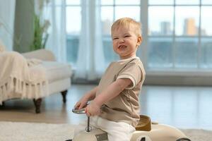 contento niño a hogar. pequeño niñito chico conducción grande Clásico juguete coche y teniendo divertida. sonriente niño jugando a hogar. bebé chico jugando con juguete en vivo habitación adentro. foto