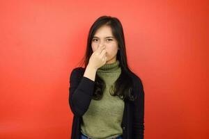 Smelling something stinky and disgusting Of Beautiful Asian Woman Isolated On Red Background photo