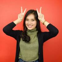 Showing Peace Sign or Victory Sign Of Beautiful Asian Woman Isolated On Red Background photo