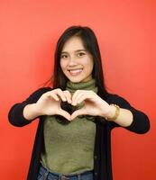 Smiling looking at camera and Showing Love Sign Of Beautiful Asian Woman Isolated On Red Background photo