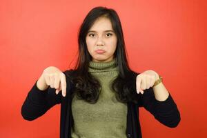 Pointing down and sad face looking at camera Of Beautiful Asian Woman Isolated On Red Background photo