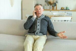 Happy middle aged senior man talking on smartphone with family friends. Older mature grandfather with cell phone talking with grown up children, resting at home. Older generation modern tech usage. photo