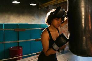 mujer yo defensa niña fuerza. africano americano mujer combatiente descansando después lucha formación en boxeo anillo. niña cansado después puñetazos boxeo bolsa. formación día en gimnasia, fuerza ajuste cuerpo rutina de ejercicio formación foto