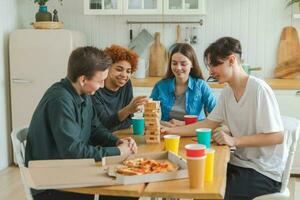 Home party. Friends spending time together playing in board game crash wooden tower at home. Happy diverse group having fun together indoor. Mixed race young buddies best friends enjoying weekend. photo