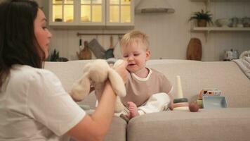 Happy family at home. Mother and baby boy playing with toys in couch at home indoors. Little toddler child and babysitter nanny having fun together. Young woman mom kid son rest in living room. photo