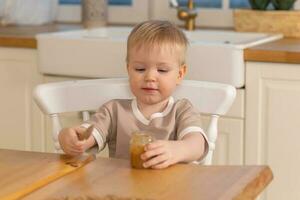 Happy family at home. Baby boy feeding himself in kitchen. Little boy with messy funny face eats healthy food. Child learns eat by himself holding spoon. Self feeding. photo