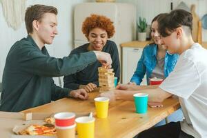 Home party. Friends spending time together playing in board game crash wooden tower at home. Happy diverse group having fun together indoor. Mixed race young buddies best friends enjoying weekend. photo