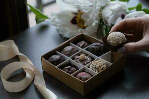 Chocolate craft candy in female hand and candy box. Healthy sweets concept photo