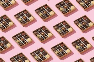 Pattern made from box with chocolate craft candies with nuts inside on pink background photo