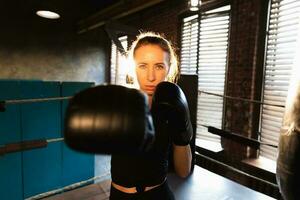 mujer yo defensa niña fuerza. fuerte mujer combatiente puñetazos con boxeo guantes a cámara. sano fuerte niña puñetazos formación puñetazos mirando concentrado derecho. ajuste cuerpo ejercicio. foto