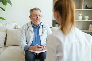 Senior man doctor examining yound woman in doctor office or at home. Girl patient and doctor have consultation in hospital room. Medicine healthcare medical checkup. Visit to doctor. photo