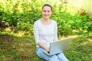 Young woman sitting on green grass lawn in city park working on laptop pc computer. Freelance business concept photo