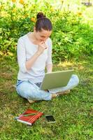 Young woman sitting on green grass lawn in city park working on laptop pc computer. Freelance business concept photo