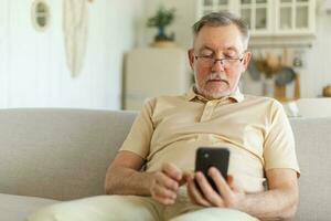 Happy middle aged senior man holding using smartphone touch screen typing scroll page. Stylish older mature beard grandfather with cell phone using internet social media apps at home. Shopping online. photo