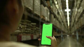 mulher mão tocante uma verde tela, rolagem, navegando para produtos em uma Smartphone dentro uma ampla armazém. video