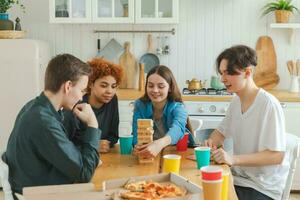 Home party. Friends spending time together playing in board game crash wooden tower at home. Happy diverse group having fun together indoor. Mixed race young buddies best friends enjoying weekend. photo