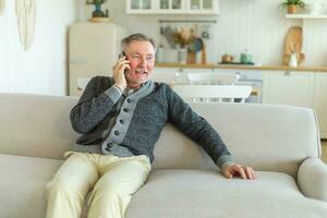 Happy middle aged senior man talking on smartphone with family friends. Older mature grandfather with cell phone talking with grown up children, resting at home. Older generation modern tech usage. photo