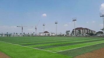 Outdoor soccer or futsal stadium with a bright synthetic grass playing field and a ball in the center. Soccer playground photo