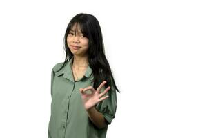 asiático niña en verde camisa en pie Okay firmar blanco antecedentes foto