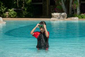 asiático pequeño niña en un traje de baño nadando a el nadando piscina foto