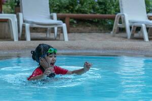 asiático pequeño niña en un traje de baño nadando a el nadando piscina foto