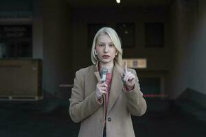 Cropped portrait of professional female reporter at work. Young woman standing on the street with a microphone in hand and smiling at camera. Horizontal shot. Selective focus on woman photo