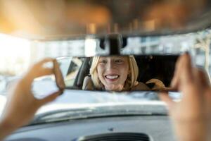 Woman hand adjusting rear view mirror of her car. Happy young woman driver looking adjusting rear view car mirror, making sure line is free visibility is good photo