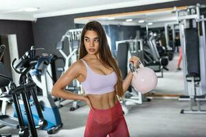 atractivo joven atleta con muscular cuerpo hacer ejercicio crossfit mujer en ropa de deporte haciendo crossfit rutina de ejercicio con tetera campana foto