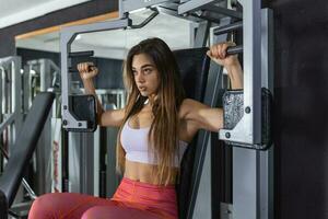 de cerca frente ver de atractivo morena trabajando fuera en un cofre prensa a un gimnasia. ella es mirando a cámara con trabajo duro, casi enojado, expresión. tonificado disparo. foto