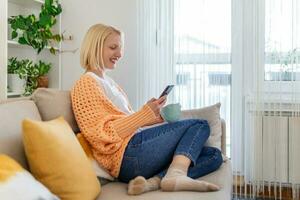 Young woman sit relax on sofa in living room browsing surfing wireless internet on smartphone, millennial girl rest on couch at home message text on modern cellphone, shopping online via website photo
