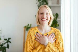 Portrait of happy millennial female volunteer holding folded hands on chest, looking at camera. Kind smiling young woman feeling thankful, showing appreciation, gratitude believe charity concept. photo