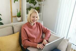 mujer joven sonriente que usa una computadora portátil en casa, mira la pantalla, chatea, usa auriculares inalámbricos y tiene una videoconferencia. tutoría de formadores de negocios por cámara web, formación en línea, concepto de e-coaching foto