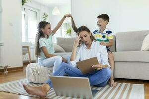 Little naughty children distracting busy young woman from work on laptop at home photo