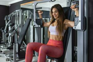 de cerca frente ver de atractivo morena trabajando fuera en un cofre prensa a un gimnasia. ella es mirando a cámara con trabajo duro, casi enojado, expresión. tonificado disparo. foto