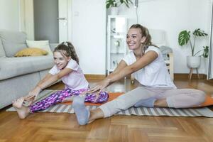 Cheerful fit female and little daughter doing lunges exercises while training together in front of laptop in modern apartment. family mother and child daughter are engaged in fitness photo
