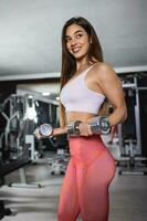 Fit strong young woman lifting weights working out with dumbbells standing with her side to the camera flexing her arm in the gym. photo