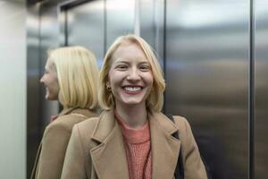 Cute blond female in trendy coat staying in lift alone and smiling, Woman in elevator photo
